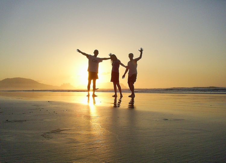 Three people at a beach during sunset.