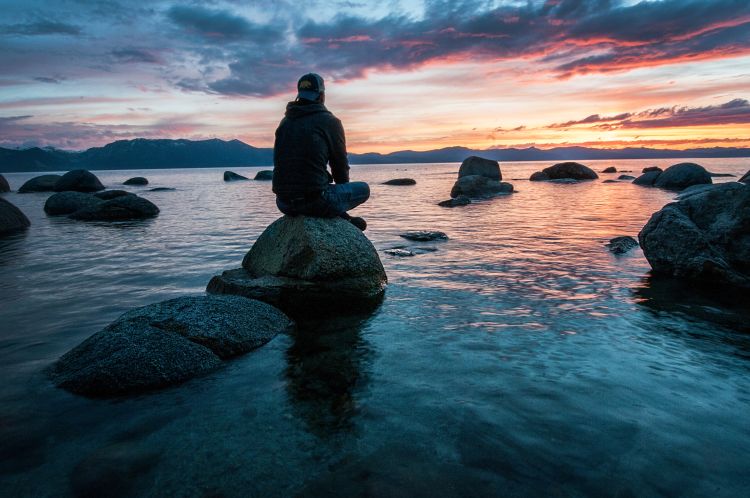 Man sitting on a rock staring at the sunrise.