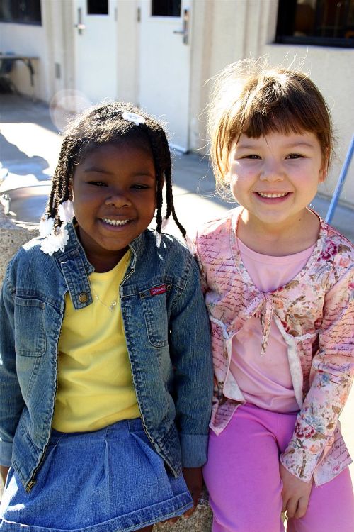 Two preschool aged children sitting together and smiling.