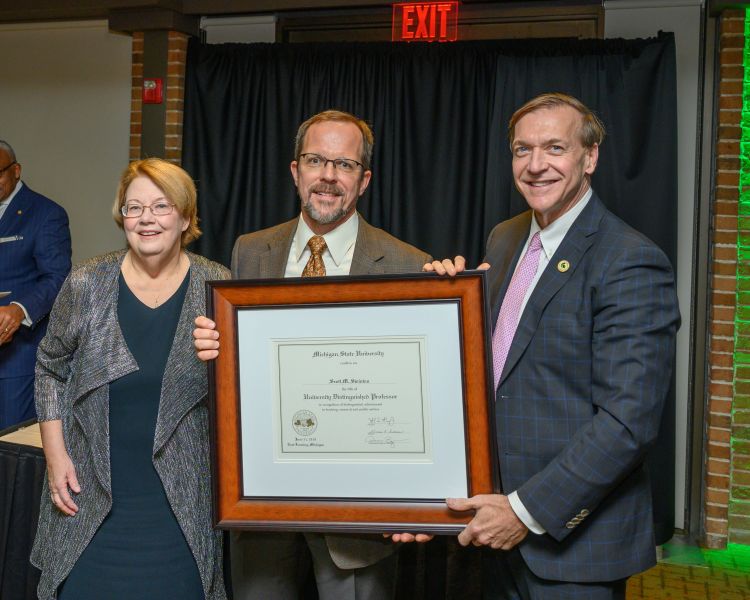 A photo of AFRE Professor Scott Swinton being given a plaque by MSU President Stanley that recognizes Scott Swinton for being named an MSU University Distinguished Professor.