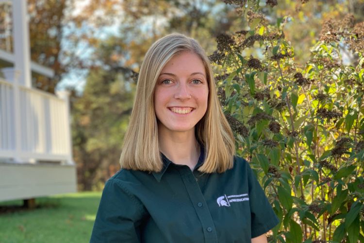 Kylie Sperow sits in front of some plants, wearing a green MSU shirt.