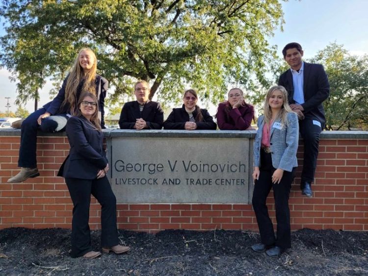 Six youth standing and sitting by a sign that says George V. Voinovich Livestock and Trade Center.