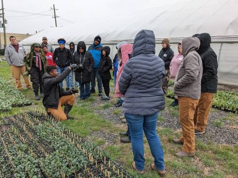 Akello Karamoko teaching the OFTP learning community about growing healthy transplants. He is seen kneeling and holding up a healthy transplant as students look on.