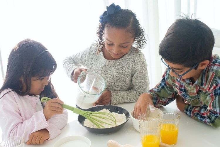 Three happy children making food at a kitchen table.