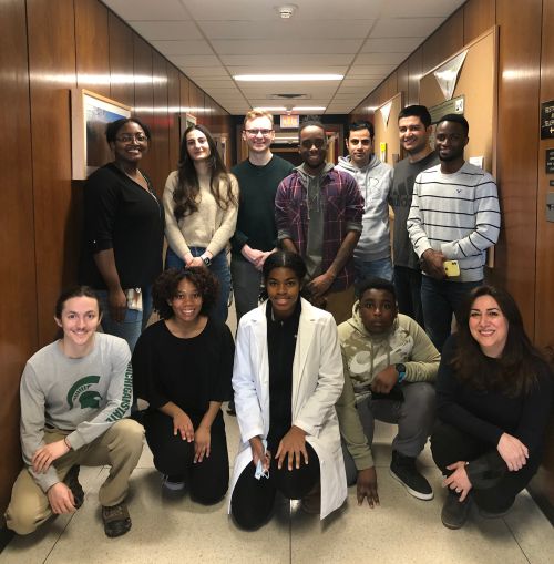 high school and graduate students posing together in a hallway, smiling