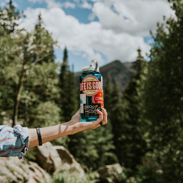 A reusable water bottle being held in front of mountains.