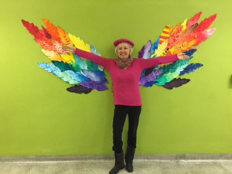 Photo of Professor April Allen standing in front of an art installation of multicolored wings