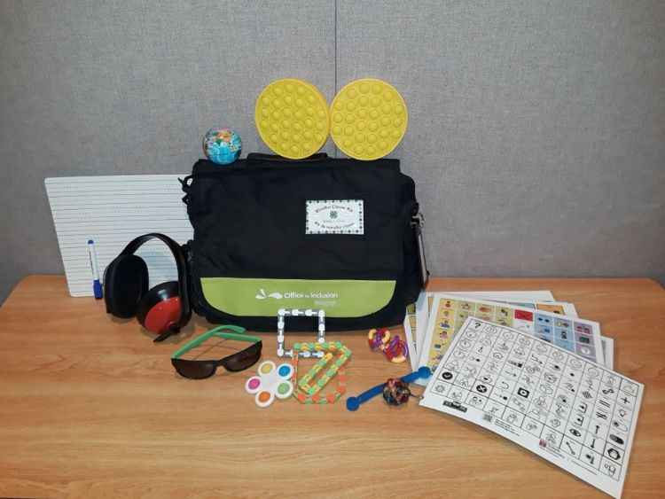 A black bag that serves as the container for the bag contents that include headphones, sunglasses, visual and textured stimulants, storyboards, dry erase board and markers.