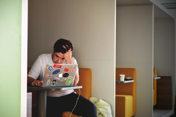 A stressed college student looking at a laptop, sitting at a booth.