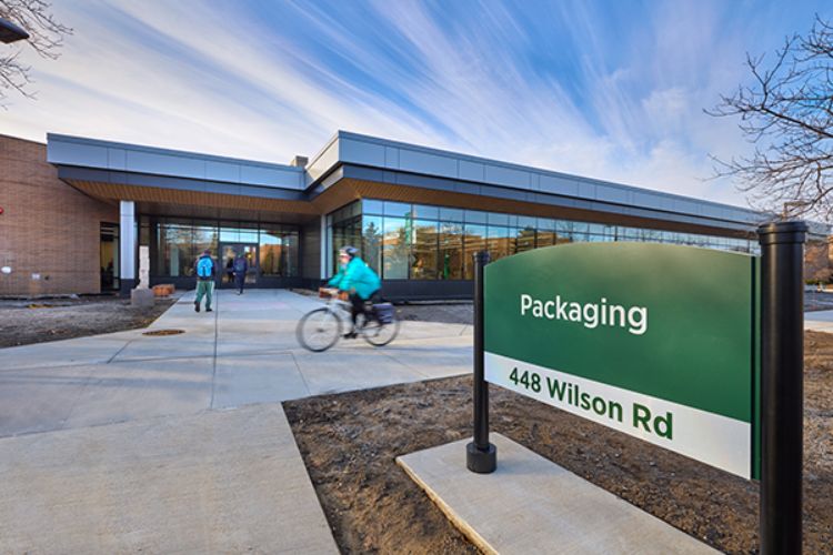 Student riding a bike by the Packaging sign and the front of the renovated Packaging building.