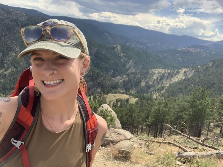 Lauren Emerick backpacking with hills and trees in the background.