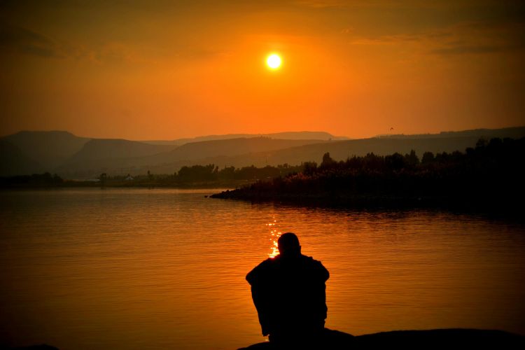 Silhouette of person sitting beside a body of water.