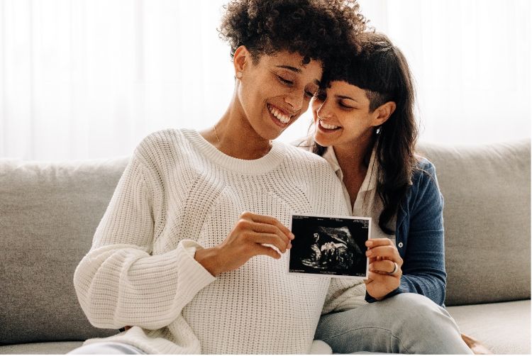 Two feminine-presenting people look at an ultrasound while smiling.
