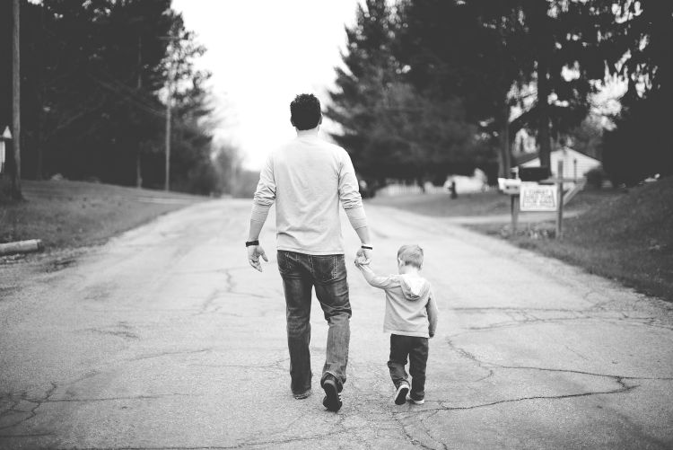 Father holding a young boy's hand walking down the street.
