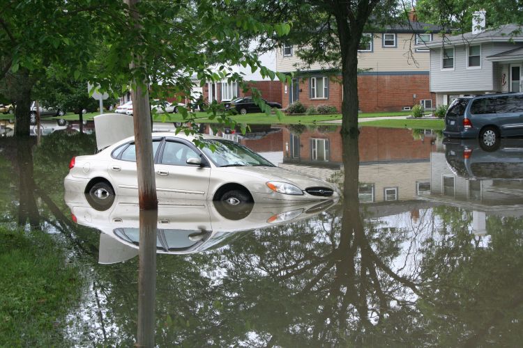 A car is shown on a flooded street in the city of Dearborn Heights. The water reaches halfway up the tires and covers the front bumper.