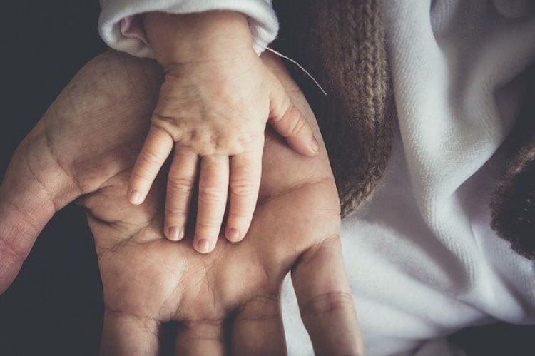 A father's palm facing up with a baby's hand in the father's palm.