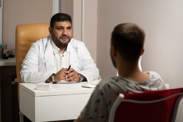 A doctor speaking with a patient, both seated at a desk.