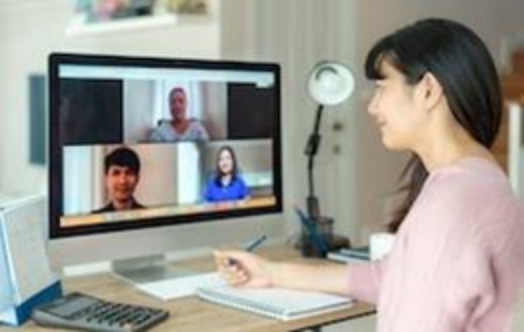 A women taking notes at her computer during a virtual meeting.