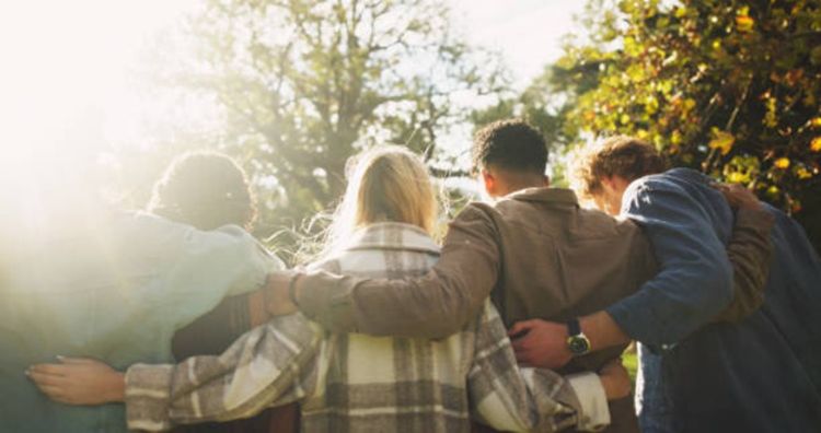 A group shot from behind of young people with their arms outstretched across one another's backs.