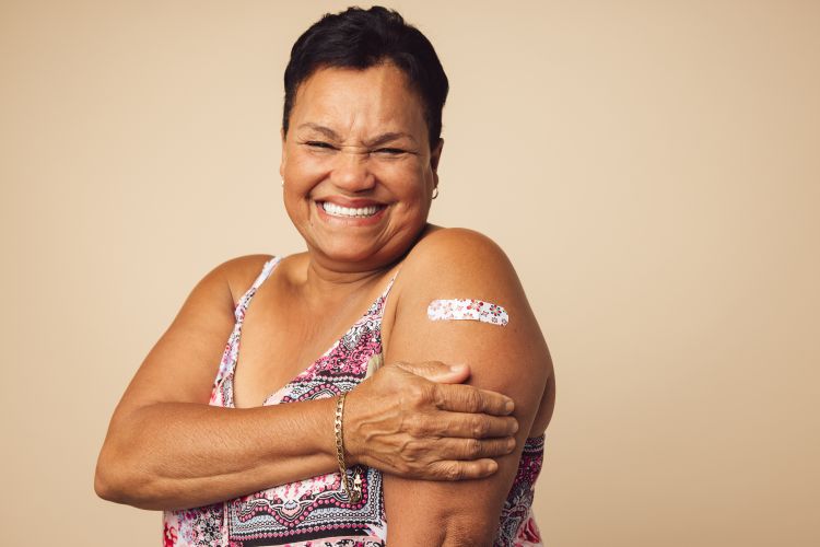 A photo of a person smiling after receiving a vaccination and showing their bandage to the camera.
