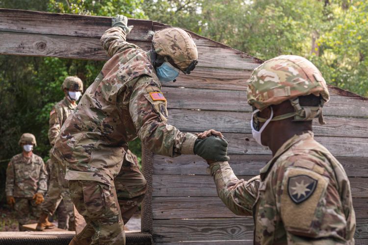 A soldier in a mask offering a hand to another soldier in a mask.