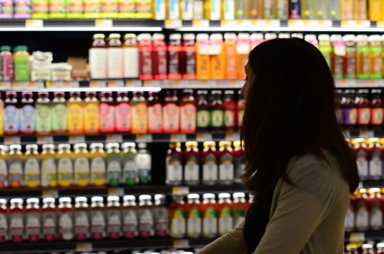 Person pushing grocery cart in grocery store aisle looking at beverage display options.