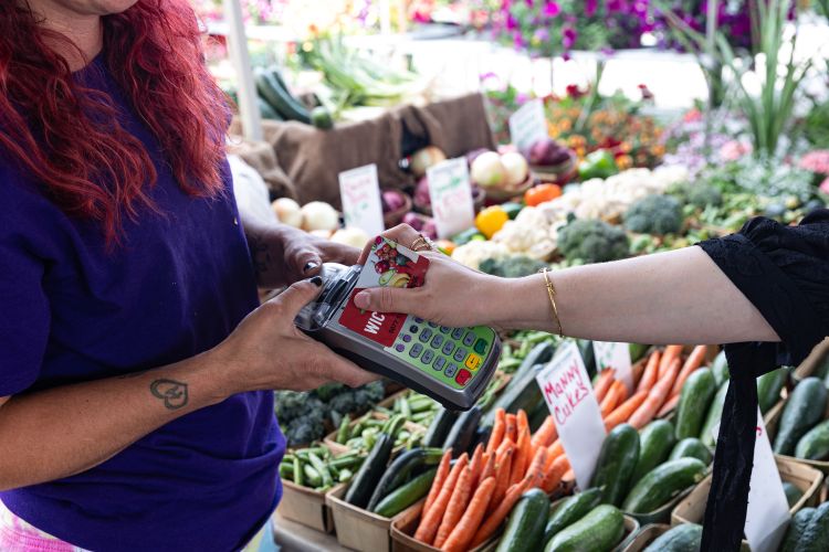 A person uses their WIC card to make a purchase at a farmer's market.