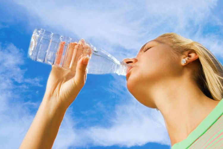 A young woman drinking water outside on a sunny day.