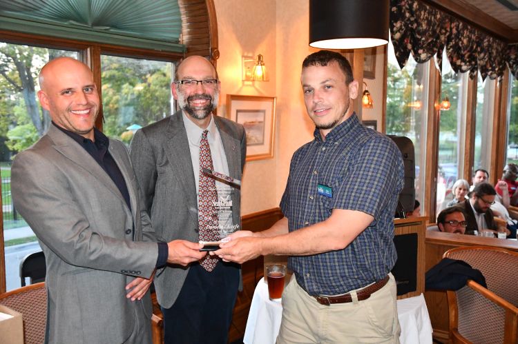 Three men standing in front of a podium. Dr. Dan O’Keefe is handed a plaque that was the Great Lakes Sea Grant Network’s mid-career award from two Sea Grant program leaders on behalf of the network.