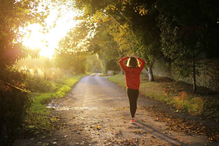 Woman walking down a dirt path surrounded by trees.