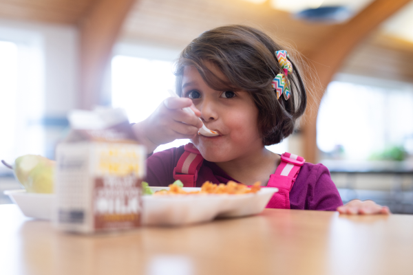 Young girl eats food from a tray at a school cafeteria table