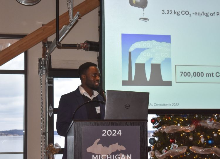 MSU PhD Student, Manasseh Agbedam, standing at a podium with a big screen behind him. timber