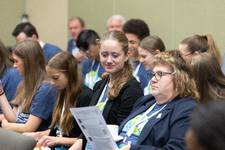 Young people sitting in a crowd in a room.