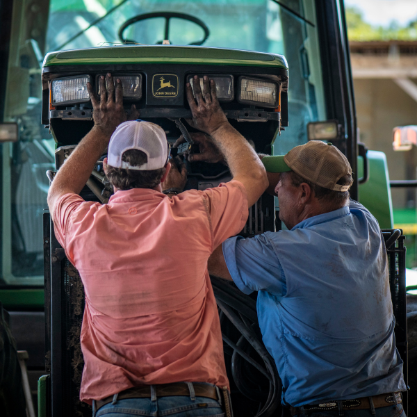 Two workers work together to repair a tractor.