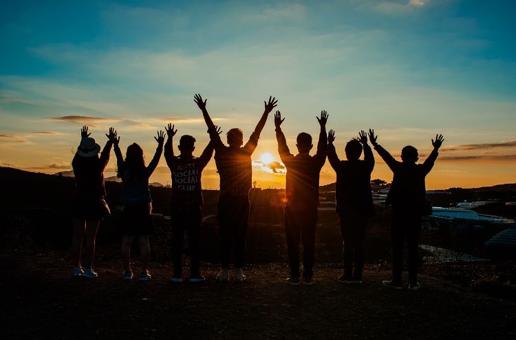 Silhouettes of people with their hand in the air and the sun behind them.