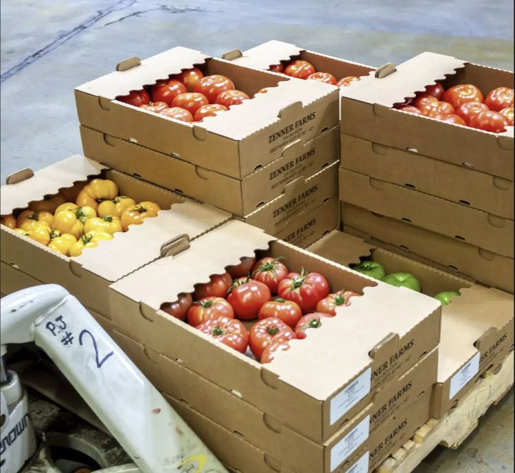 Pallet boxes full of red, yellow, and green tomatoes await distribution at a food hub.