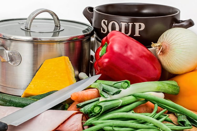 Soup vegetables and other ingredients with soup bowl, chef's knife and pot.