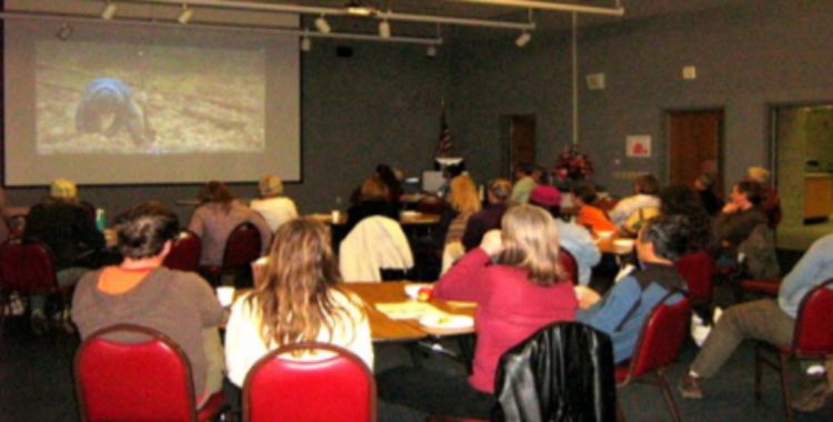 Group of people sitting in room watching a slide show.