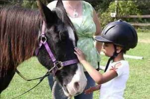 Youth wearing a riding helmet, petting a pony.