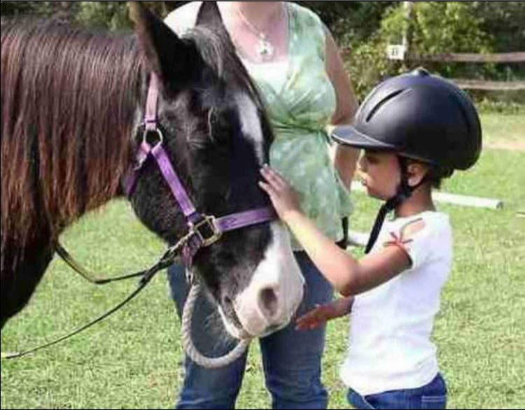 Youth wearing a riding helmet, petting a pony.