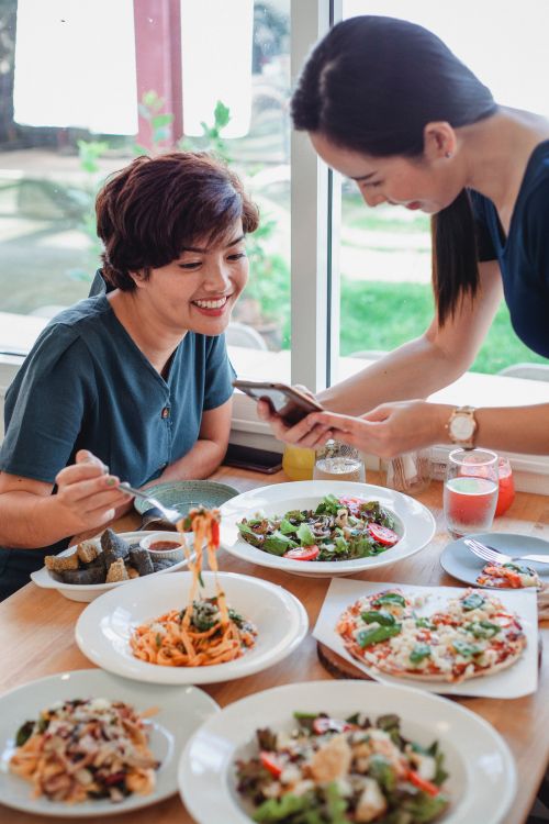 Two women looking at a smartphone over a table full of different dishes.