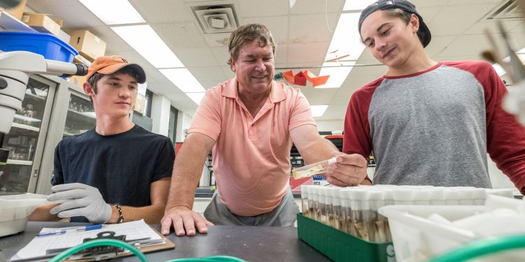 Larry Gut with students leaning over a table.