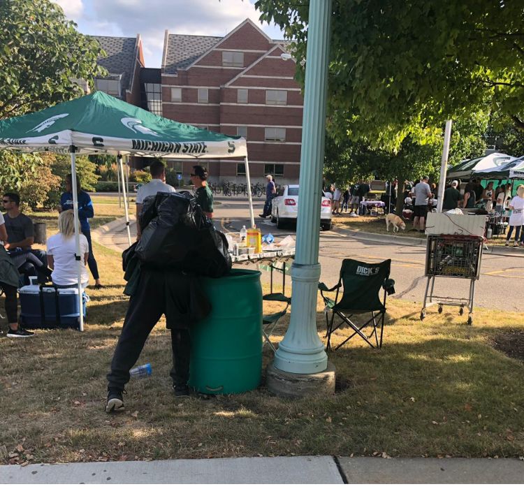 A canner collecting cans from a trash bin at a MSU football tailgate in 2019.