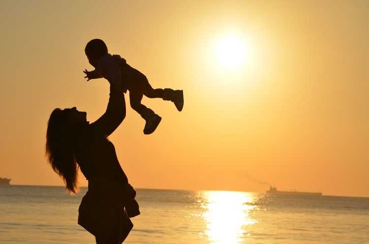 A mother lifting her child at sunset.
