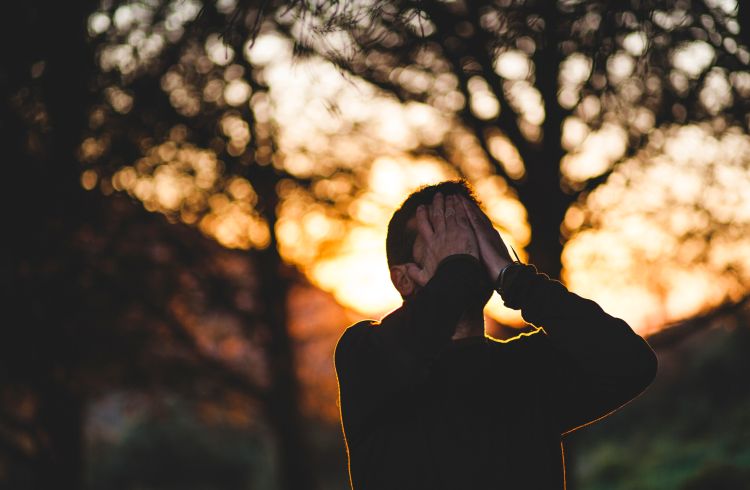 Man with both hands to his face in front of a sunset.