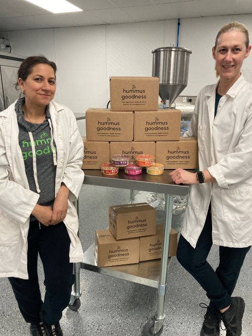 two women in lab coats standing near a cart with boxes