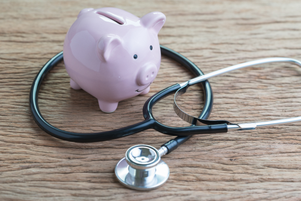 stethoscope with pink piggy bank on wooden table