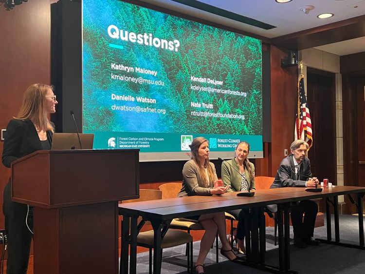 Kathryn Maloney from the FCCP standing at a podium presenting to an audience. On the right side, panel speakers (Kendall DeLyser, Danielle Watson, and Nathan Truitt) are sitting down at a table facing the audience.