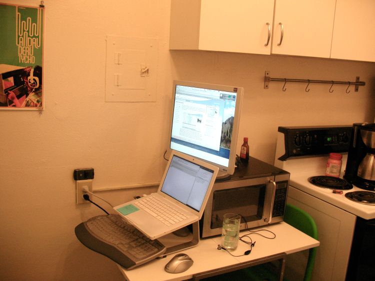 Computer and monitor sitting on a table in a kitchen.