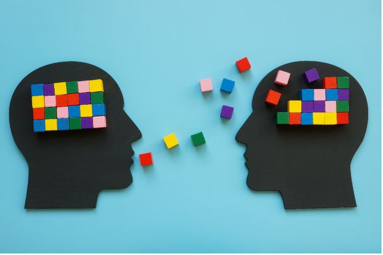 An abstract image of two silhouette heads transmitting multi-colored blocks between one another.